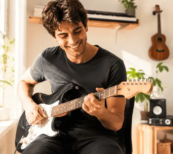 Jovem tocando guitarra em casa, representando a missão do Tocando do Zero de levar música para todos